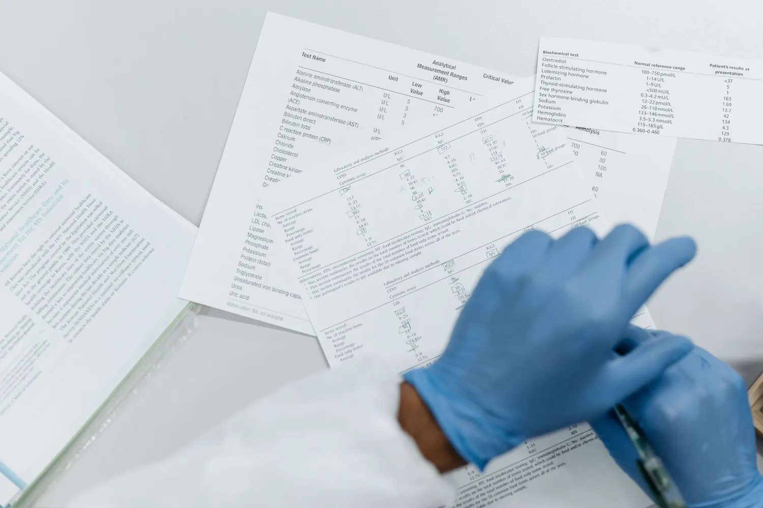 Zdravstveni delavec v rokavicah pregleduje izvide krvnih preiskav na laboratorijskih poročilih