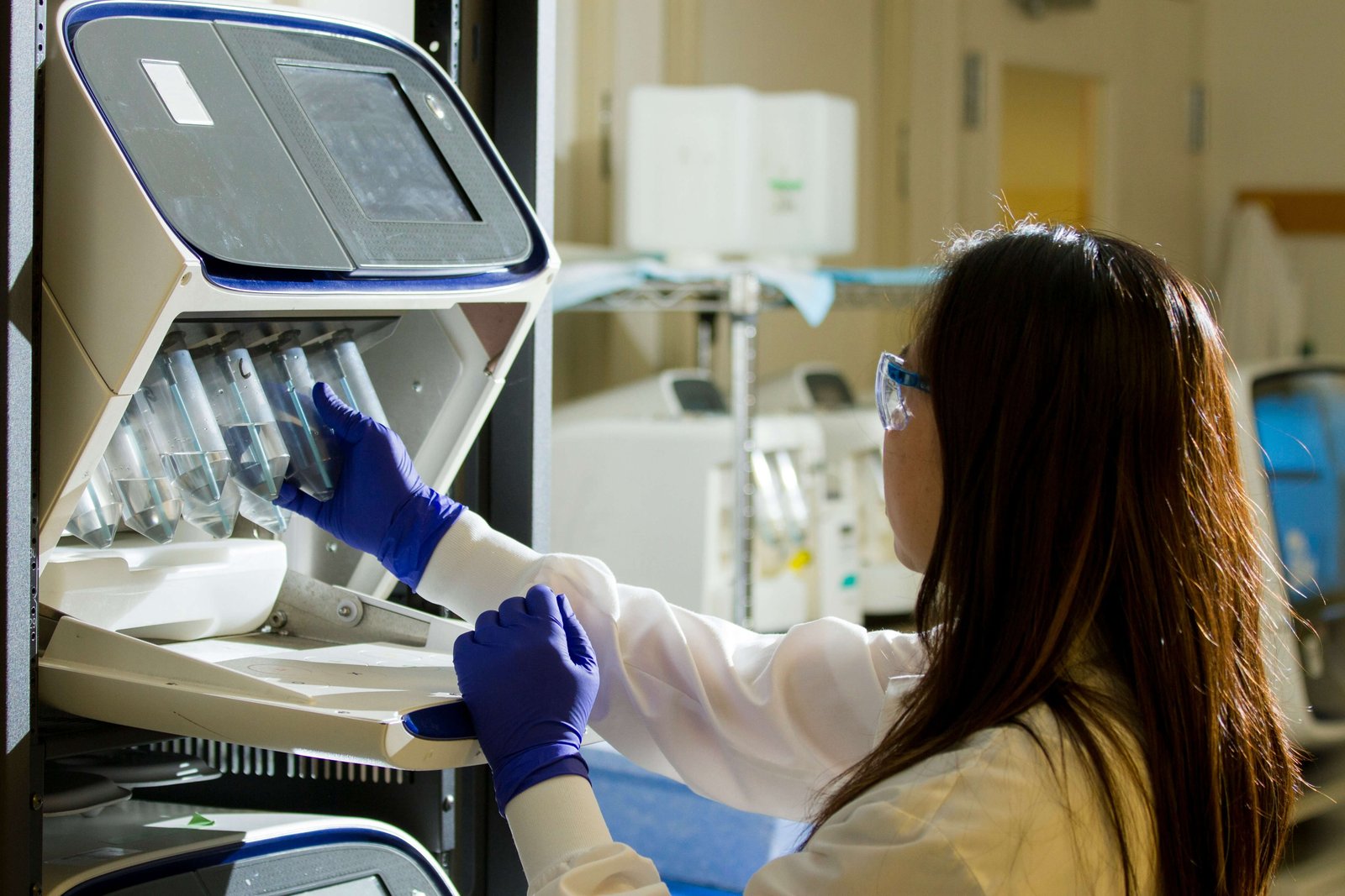 Laboratorijski znanstvenik v rokavicah in zaščitnih očalih vstavlja vzorce v napravo za genetsko analizo.