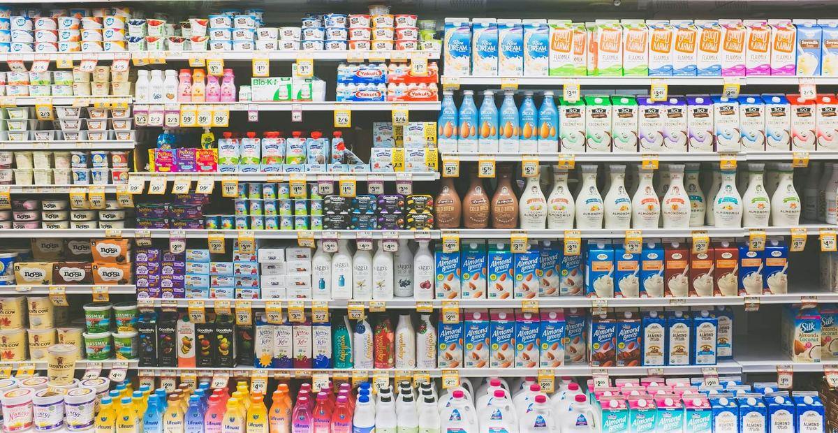 A fully stocked refrigerated supermarket aisle packed with cartons and bottles of milk, tubs of yogurt and kefir, and rows of plant-based milk cartons such as almond, coconut, oat and rice.